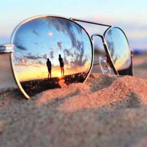 Aviator sunglasses resting in the sand reflecting a sunset